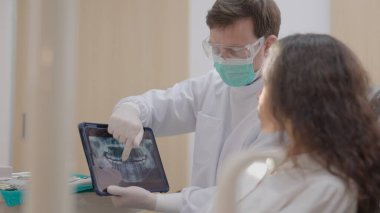 Klinikte dişçi bir hastanın dişlerini temizler..