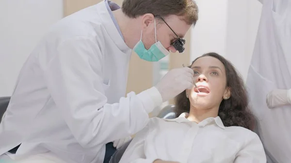 Klinikte dişçi bir hastanın dişlerini temizler..