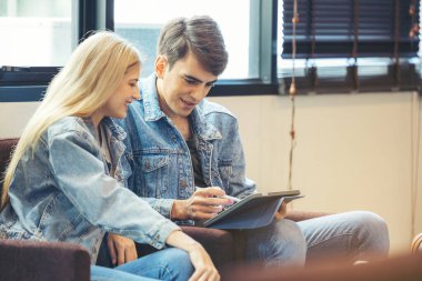 Bir çift otel lobisinde oturup tablet bilgisayara bakıyorlar..