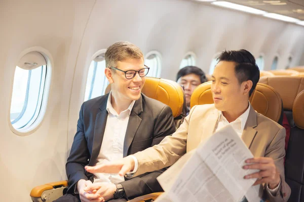 During a flight, a businessman in formal attire and glasses works with a friend near the window, business travel concept