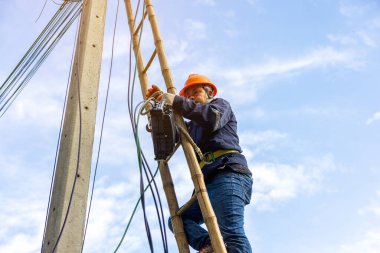 A telecoms worker is shown working from a utility pole ladder while wearing high visibility personal safety clothing, PPE, and a hard hat.	