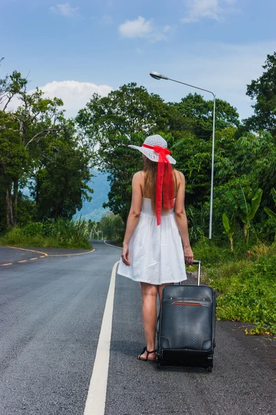 Meisje met een koffer op een verlaten weg — Stockfoto