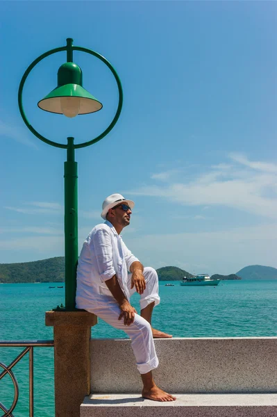 The man in a white suit and hat sitting on a rock on the sea ba — Stock Photo, Image