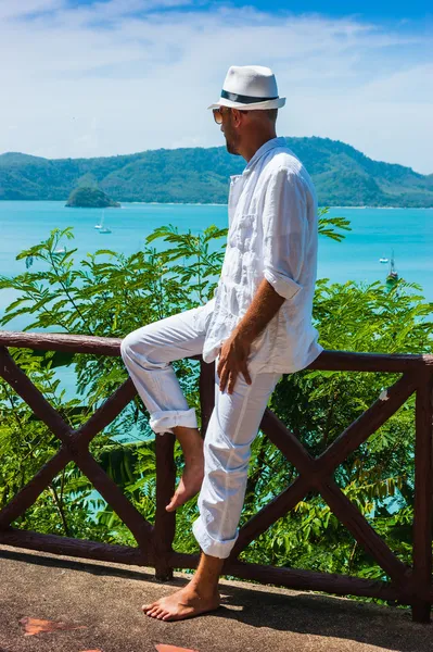 Człowiek w białym garniturze i kapeluszu siedzi na skale na morze ba — Zdjęcie stockowe