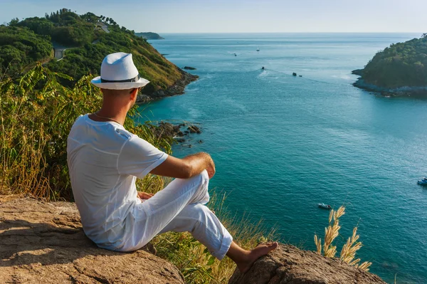 El hombre con un traje blanco y sombrero sentado en una roca en el mar ba —  Fotos de Stock