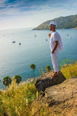Beyaz takım elbise ve şapka deniz ba bir kayaya oturan adam