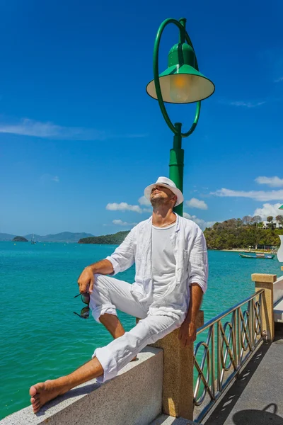The man in a white suit and hat sitting on a rock on the sea ba — Stock Photo, Image