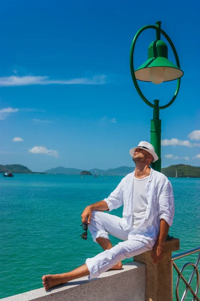 The man in a white suit and hat sitting on a rock on the sea background — Stock Photo, Image