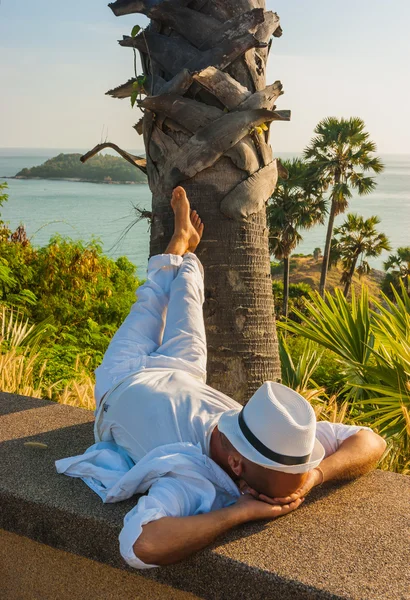 The man in a white suit and hat sitting on a rock on the sea background — Stock Photo, Image