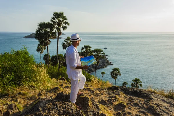 The man in a white suit and hat sitting on a rock on the sea background — Stock Photo, Image