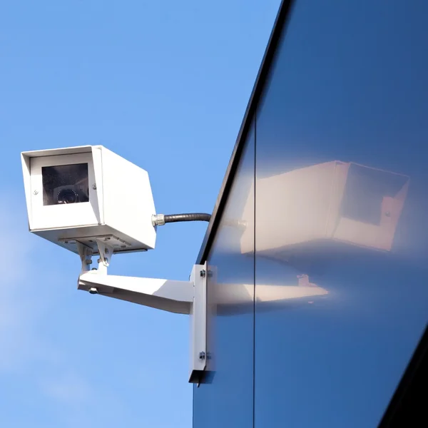 Security camera reflected on shiny building facade Stock Picture