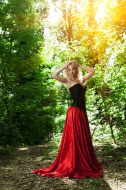 Siyah korseli, kırmızı etekli, ormanda poz veren güzel, seksi sarışın.