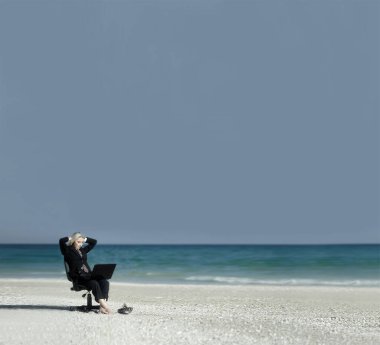 Kumsaldaki ofis sandalyesi ve dizüstü bilgisayarı olan bir iş kadını.