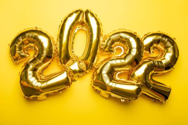2022 Altın folyo balonundan sarı arkaplan fotoğrafına yeni yıl kavramı