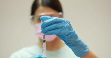 Koruyucu eldivenler giyen ve cam şişeyi iğne sıvısıyla tutan bir doktor. Grip ve koronavirüse karşı aşı. 4K stok video