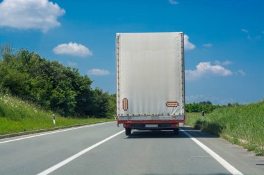 Kırsal alanda asfalt yolda beyaz nakliye kamyonları sürüyor.