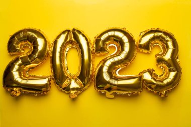 2023 concept Happy New Year from golden foil balloon on yellow background
