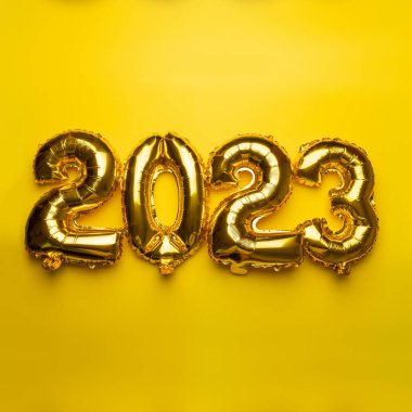 2023 concept Happy New Year from golden foil balloon on yellow background