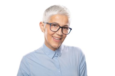 Uzman! Güzel, gülümseyen, yaşlı, gözlüklü, mavi gömlekli, beyaz saçlı ve gözlüklü bir iş kadını gri arka planda poz veriyor.
