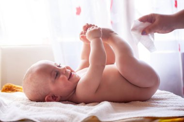 Anne gülümseyen bebeğin teniyle ilgilenir ve bebeğin poposunu suyla ve ıslak mendille siler.