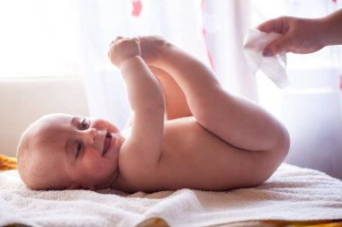 Anne gülümseyen bebeğin teniyle ilgilenir ve bebeğin poposunu suyla ve ıslak mendille siler.