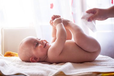 Anne gülümseyen bebeğin teniyle ilgilenir ve bebeğin poposunu suyla ve ıslak mendille siler.