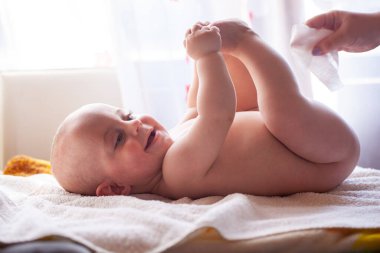 Anne mutlu bebeğin cildine bakar ve bebeğin poposunu suyla ve ıslak mendille siler.