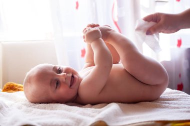 Anne gülümseyen bebeğin derisine bakar ve bebeğin poposunu suyla ve ıslak mendille siler.