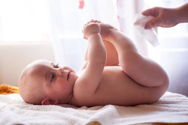 Anne mutlu bebeğin cildine bakar ve bebeğin poposunu suyla ve ıslak mendille siler.