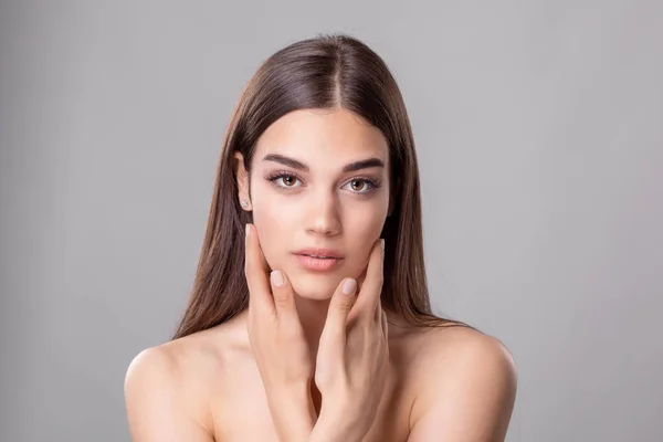 Beautiful young woman with clean perfect skin. Portrait of beauty model with natural nude make up and touching her face. Spa, skincare and wellness. Close up, copyspace.