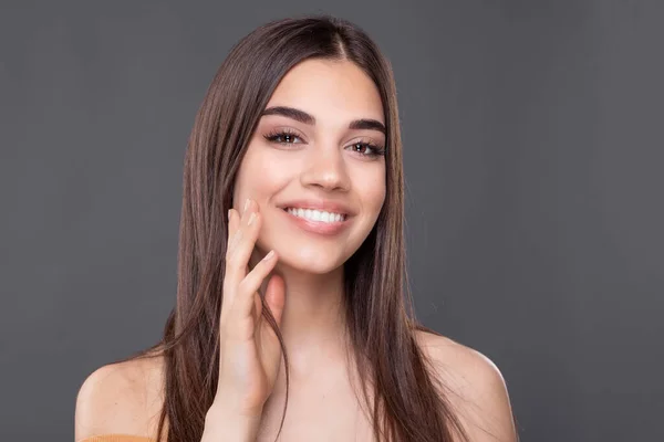 Beautiful young woman with clean perfect skin. Portrait of beauty model with natural nude make up and touching her face. Spa, skincare and wellness. Close up, copyspace.