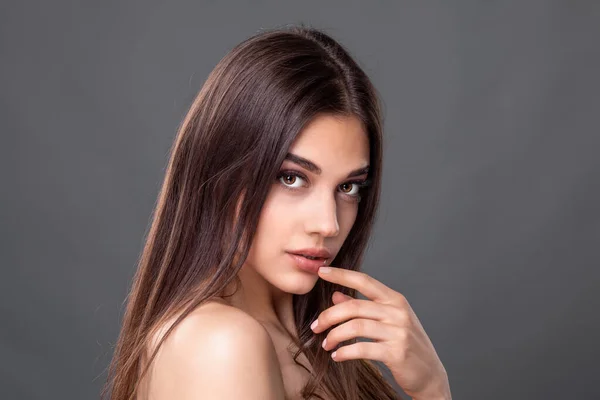 Seductive look. Beautiful young woman with clean perfect skin. Portrait of beauty model with natural nude make up and touching her face. Spa, skincare and wellness. Close up, copyspace.