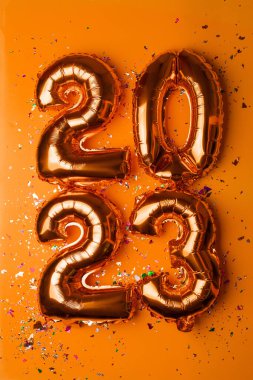 2023 concept Happy New Year from golden foil balloon and confetti on yellow background stock photo
