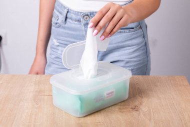 Kolsuz tişörtlü kadın tek kullanımlık paketten ıslak mendil alıyor. Hijyen prosedürü ve bulaşıcı hastalıkların önlenmesi.
