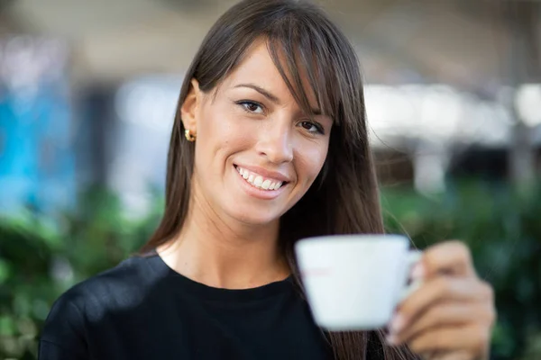 Beautiful smiling woman in black shirt drinking coffee in garden of cafe