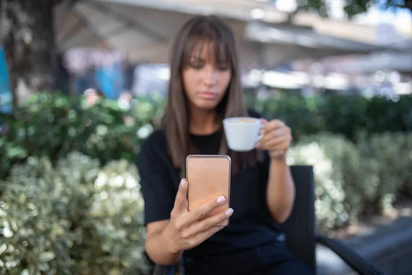 Morning in cafe - attractive woman in black drinkin coffe and make selfie photo for social networks. stock photo