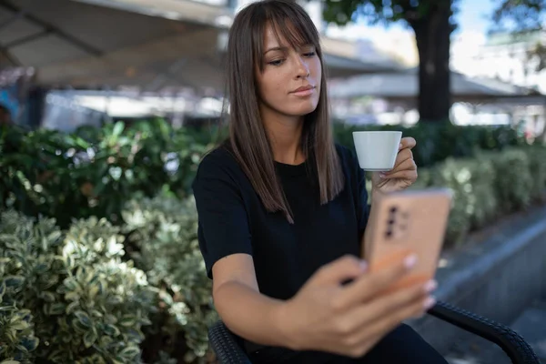 Morning in cafe - attractive woman in black drinkin coffe and make selfie photo for social networks. stock photo