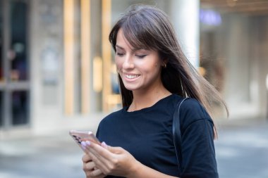 Siyah tişörtlü güzel bir kadın şehir merkezindeki caddede akıllı telefondan mesaj atıyor.