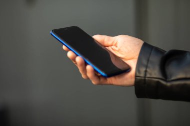 Cep telefonunu elinde tutan genç ve modern bir adamın internet uygulaması üzerinden sohbet ederken yakın plan fotoğrafı.