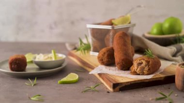 Meat croquets with rosemary leaves and lemons on wooden cutting board in a kitchen counter top.