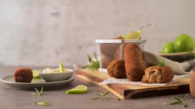Meat croquets with rosemary leaves and lemons on wooden cutting board in a kitchen counter top.