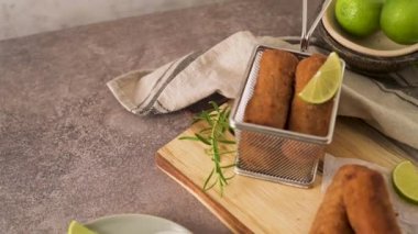 Meat croquets with rosemary leaves and lemons on wooden cutting board in a kitchen counter top.