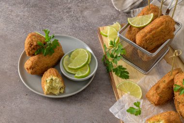 Meat croquets with rosemary leaves and lemons on wooden cutting board in a kitchen counter top.