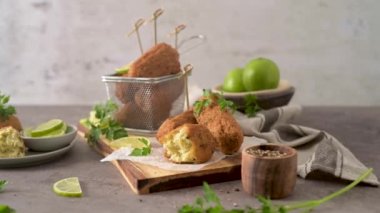 Meat croquets with rosemary leaves and lemons on wooden cutting board in a kitchen counter top.