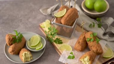 Meat croquets with rosemary leaves and lemons on wooden cutting board in a kitchen counter top.