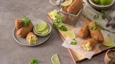 Meat croquets with rosemary leaves and lemons on wooden cutting board in a kitchen counter top.