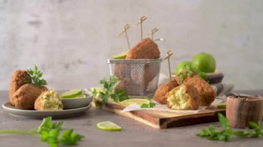 Meat croquets with rosemary leaves and lemons on wooden cutting board in a kitchen counter top.