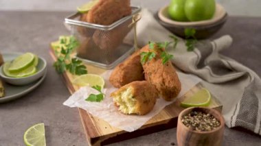 Meat croquets with rosemary leaves and lemons on wooden cutting board in a kitchen counter top.