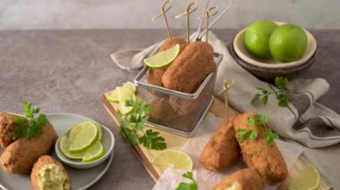 Meat croquets with rosemary leaves and lemons on wooden cutting board in a kitchen counter top.