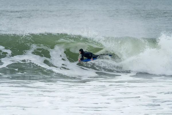 Bodyboarder performing a tube trick surfing ocean wavesurfing ocean wave on a cloudy winter day.